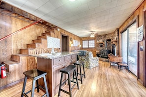 A kitchen with wooden walls, a central island, bar stools, a fireplace, and a window.