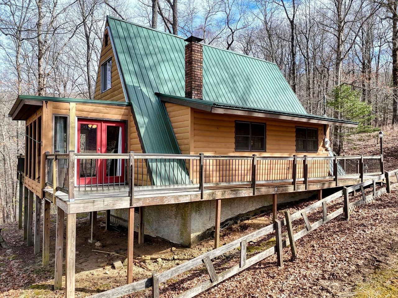 A cabin with a green roof, a red door, and a wooden deck.