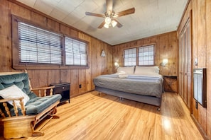 A wooden-paneled room with a bed, a chair, and a ceiling fan.