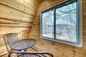 A wooden cabin interior with a large window, a metal table, and a chair.