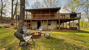 A two-story wooden cabin with a deck, outdoor seating, and a fire pit.