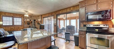 A kitchen with granite countertops, stainless steel appliances, wooden cabinets, and a large island with bar stools.