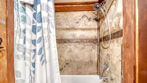 Ein Badezimmer mit Dusche, Badewanne und einem Vorhang mit Blätermotiv.