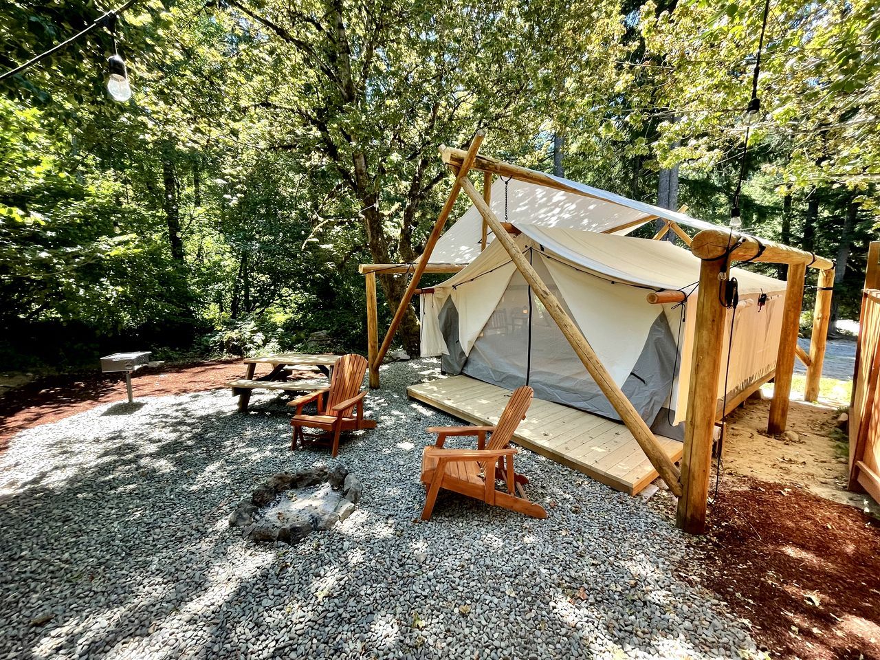 Une tente dotée d’une structure en bois et d’un toit en toile, entourée de gravier et de chaises en bois.