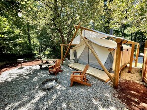 A tent with a wooden frame and a canvas roof, surrounded by gravel and wooden chairs. - Woodsmen (Idleyld Park)