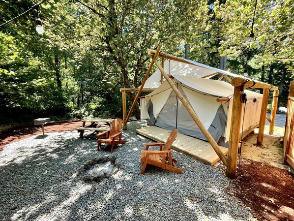 A tent with a wooden frame and a canvas roof, surrounded by gravel and wooden chairs.