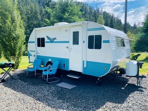 A recreational vehicle parked on gravel with a small table and two chairs.