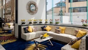 Un hall d’hôtel moderne avec un espace salon, une grande fenêtre donnant sur la ville et un miroir décoratif au mur.