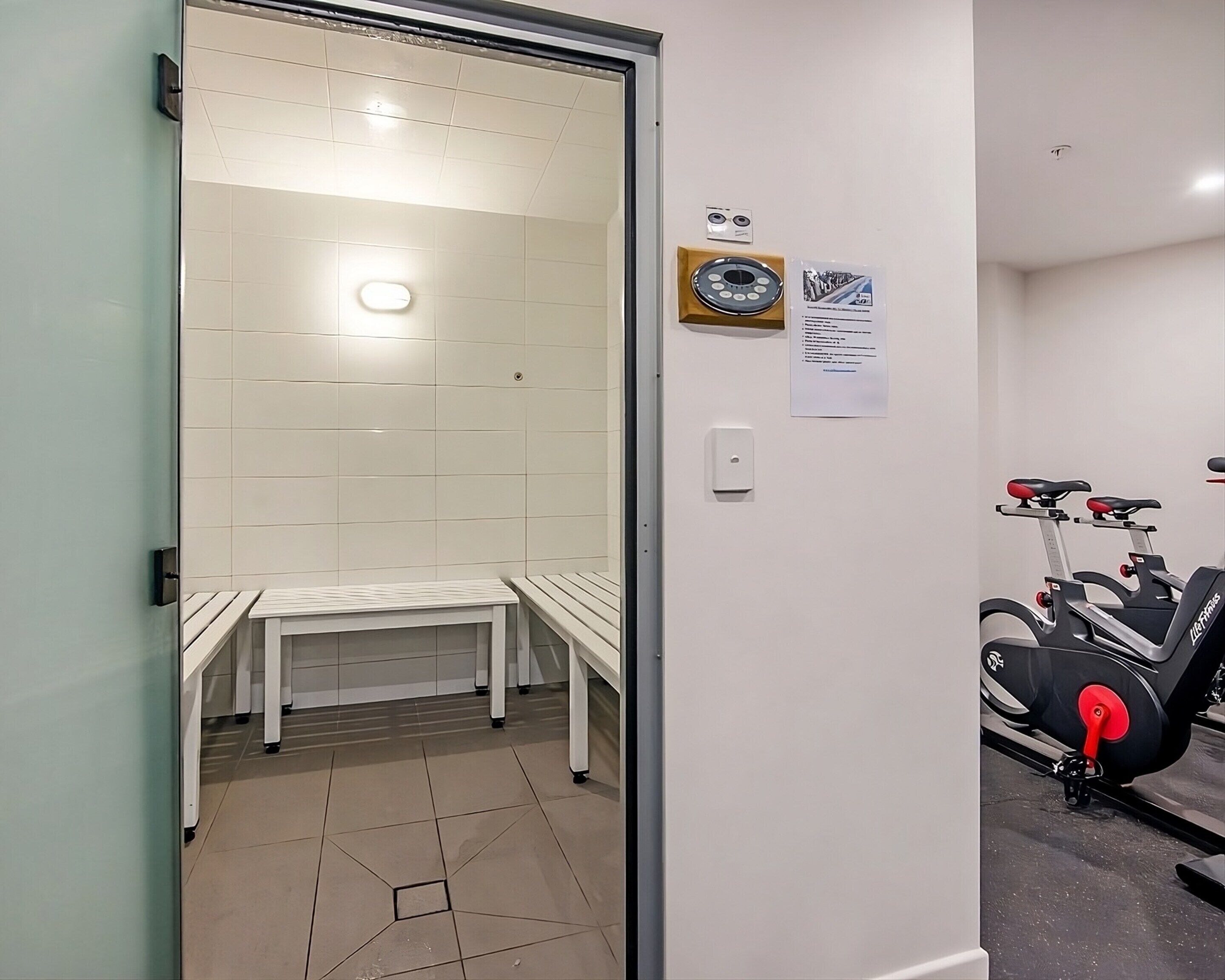 A room with a sauna, a bench, a wall-mounted exercise bike, and a small table.