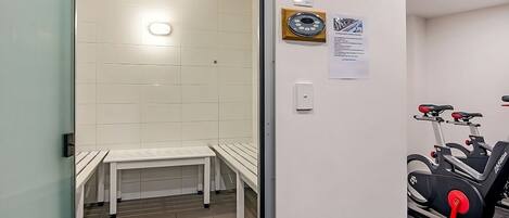 A room with a sauna, a bench, a wall-mounted exercise bike, and a small table.