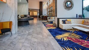 Un hall d’entrée moderne avec un sol en marbre, un comptoir d’accueil, un espace salon agrémenté d’un tapis à motifs et un grand miroir mural.