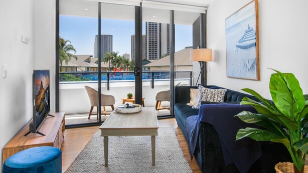 Un salon moderne comprenant un canapé, des fauteuils, une table basse et une grande fenêtre donnant sur des immeubles de grande hauteur et une piscine.