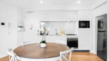 A modern kitchen with white cabinets, a round wooden dining table, and white chairs.