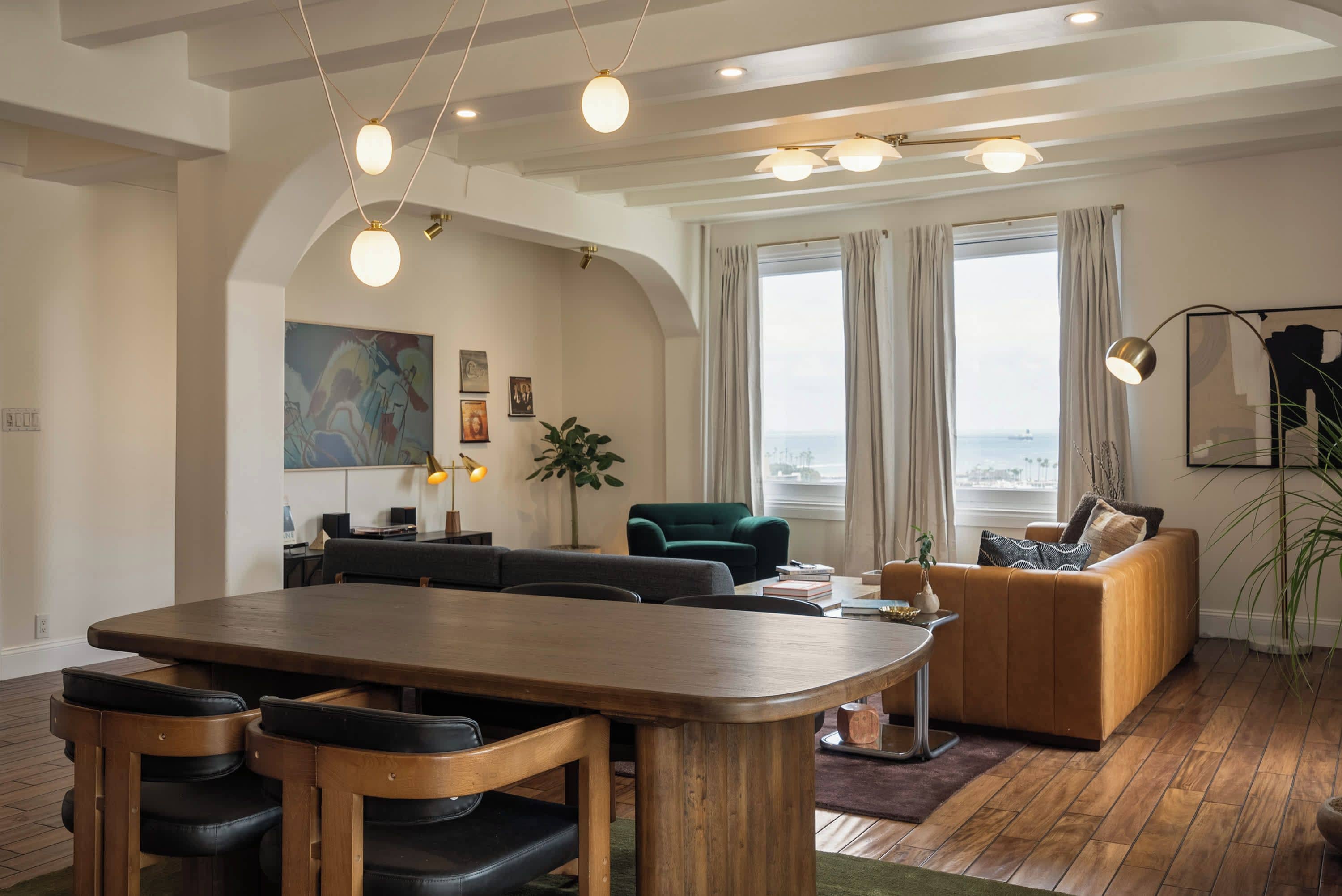 A modern living room with a wooden dining table, sofas, and a large window with curtains.