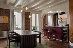 A modern kitchen with a wooden dining table, bar stools, and a built-in island. - Ocean-View 1BR Condo in Historic Cooper Arms (Long Beach)