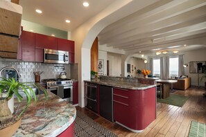 A modern kitchen with red cabinets, a granite countertop, and stainless steel appliances.