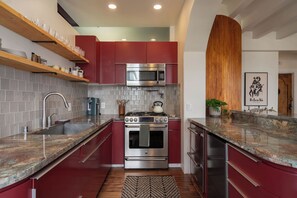 A modern kitchen with stainless steel appliances, red cabinetry, and marble countertops.