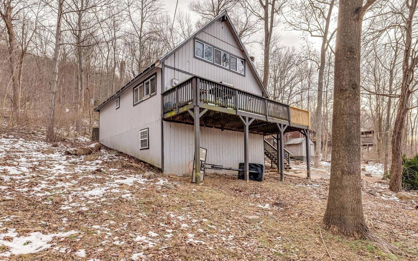 A two-story house with a balcony, surrounded by trees and a wooded area.