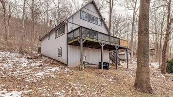 A two-story house with a balcony, surrounded by trees and a wooded area.