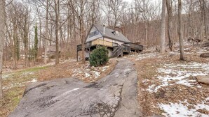 Eine Holzhütte mit einer Holzterrasse, umgeben von einem Wald mit Schneeflecken.