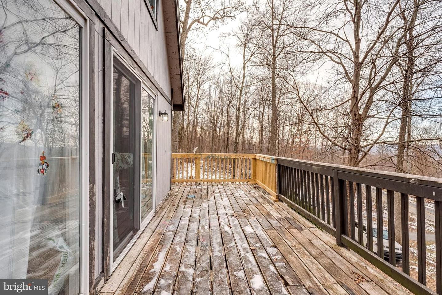 A wooden deck with a glass door leading to a room, surrounded by trees.