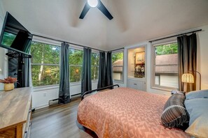 A bedroom with a bed, a TV, and a window with curtains.