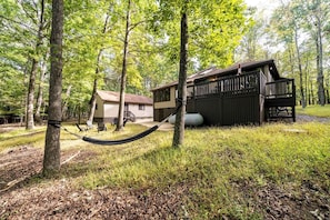 A cabin with a deck, surrounded by trees, and a hammock in the foreground.