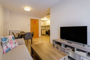 A compact living space with a sofa, a coffee table, a TV, a dining area, and a kitchen in the background.