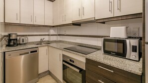 Una cocina con electrodomésticos de acero inoxidable, horno empotrado, microondas y cafetera.