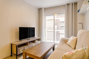 A living room with a flat-screen TV on a wooden stand, a beige sofa, and a wooden coffee table.