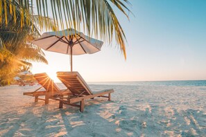 A beach with wooden lounge chairs and a palm tree.