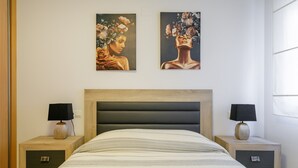 Un dormitorio con una cama, dos mesitas de noche, un cabecero y dos cuadros colgados en la pared.