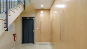 Un pasillo con una escalera, un extintor y una puerta con pantalla digital.