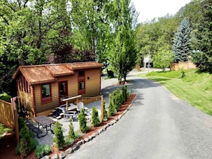 A cabin with a gravel driveway, a patio with outdoor furniture, and a forested backdrop.