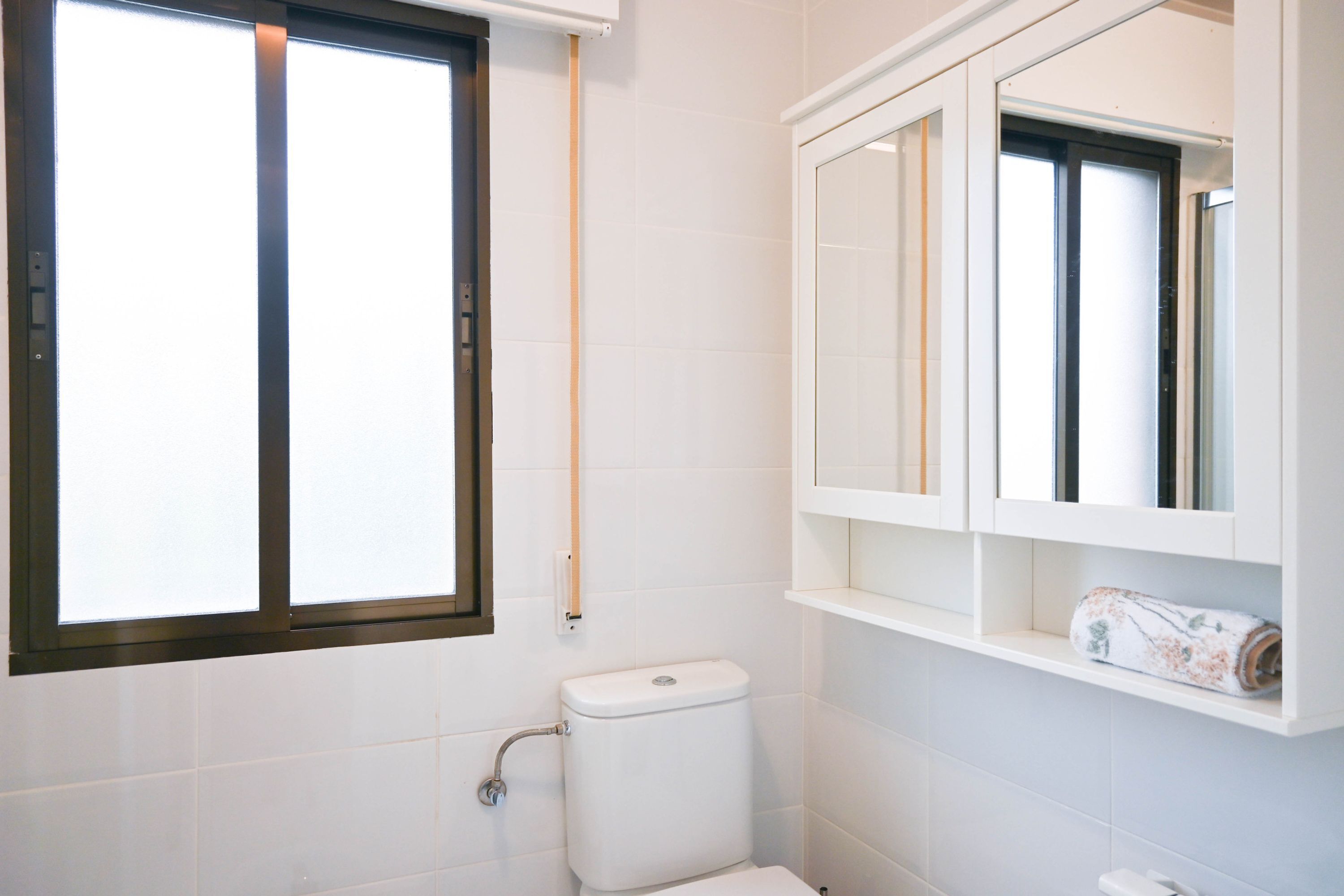 A bathroom with a toilet, a window, and a cabinet with shelves.