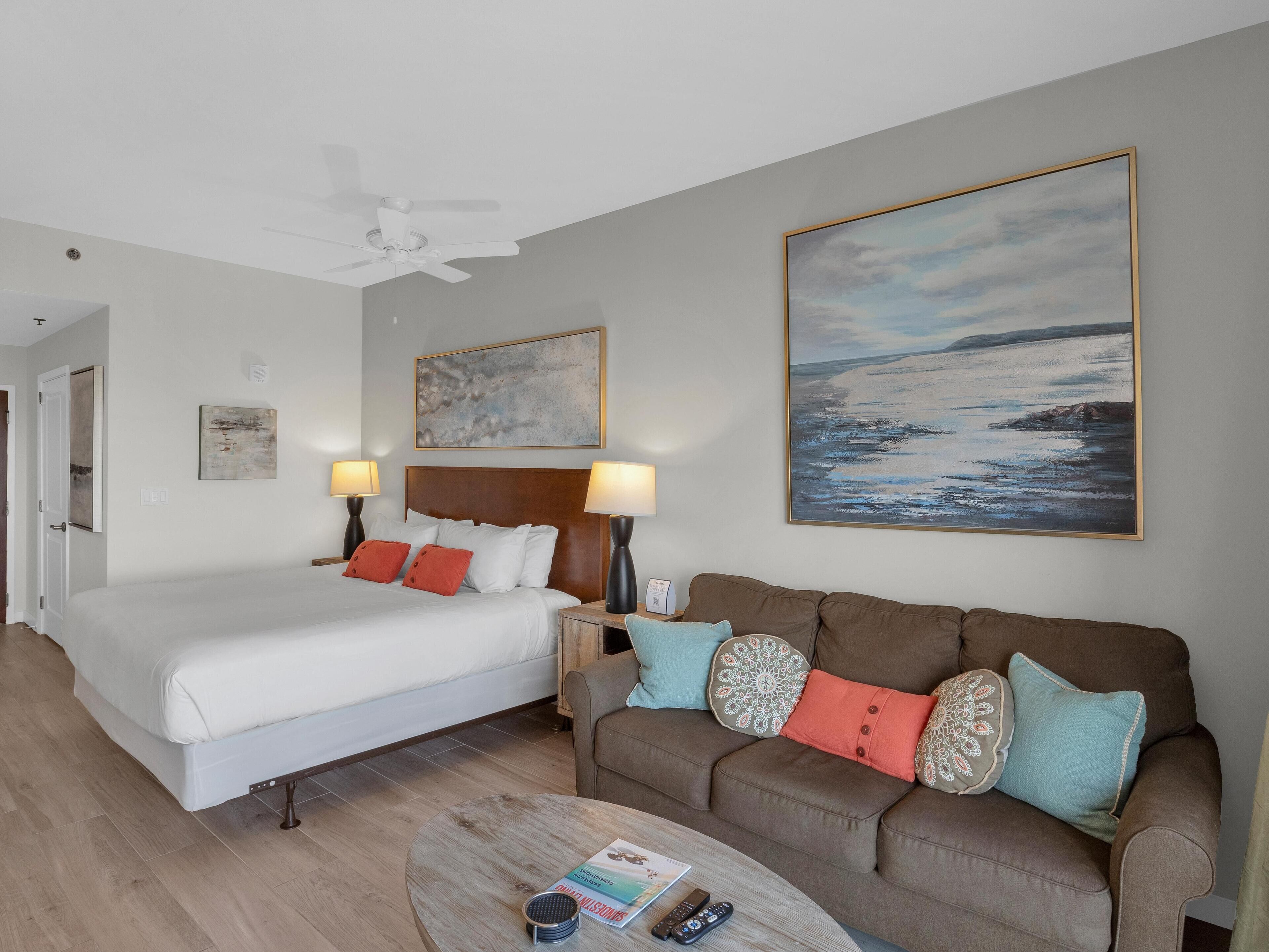 A hotel room with a bed, a sofa, a coffee table, and artwork on the walls.