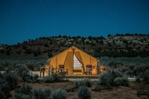 A tent-like structure with a central entrance, surrounded by sparse vegetation, set against a night sky.