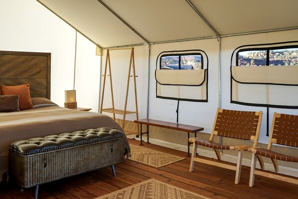 A tent-style room with a bed, a bench, a chair, a small table, and a window.