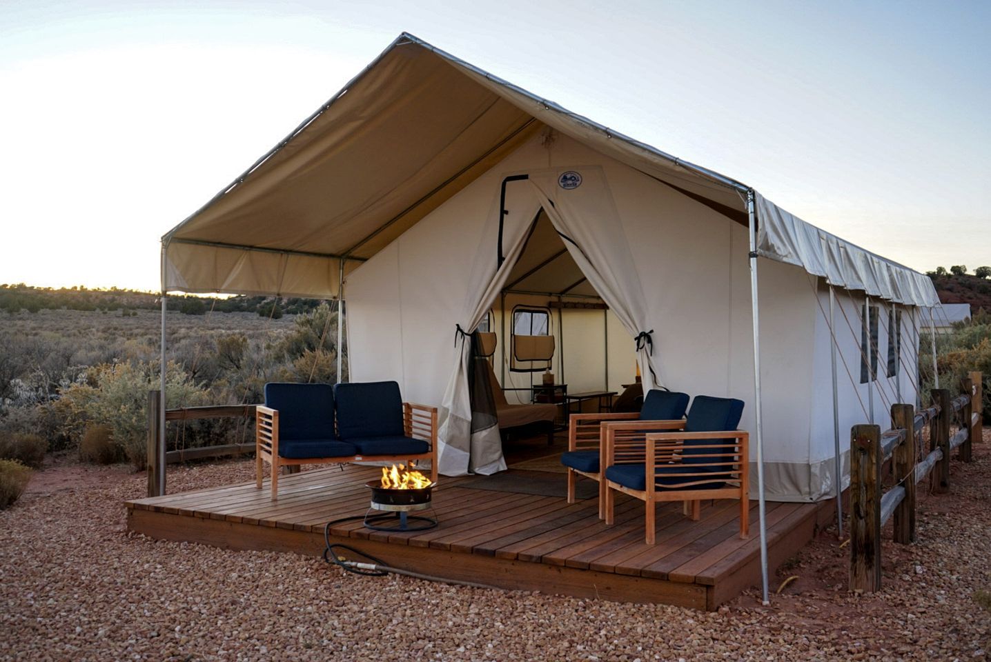 A tent with a wooden deck, two sofas, a fire pit, and a view of the surrounding landscape.