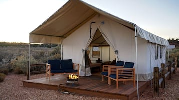 A tent with a wooden deck, two sofas, a fire pit, and a view of the surrounding landscape.