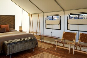 A tent-style room with a bed, a bench, a chair, a small table, and a window.