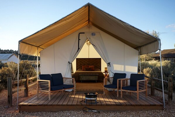 A tent with a bed, two chairs, a small table, and a fire pit.