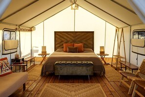 Habitación con tienda de campaña, una cama grande, dos mesitas de noche, una lámpara colgante y una silla colgante.