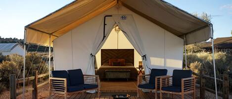 A tent with a bed, two chairs, a small table, and a fire pit.