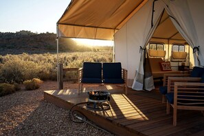A tent with two chairs, a table, and a fire pit on a wooden deck.