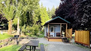 Une petite cabane avec une véranda, une table de pique-nique et une clôture en bois.
