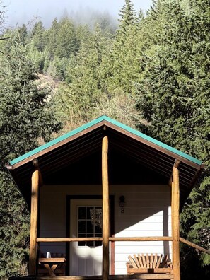 A wooden cabin with a pitched roof, a front door, and a bench outside.