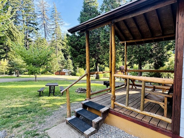 A wooden deck with steps leading to a covered area, surrounded by trees and a picnic table.