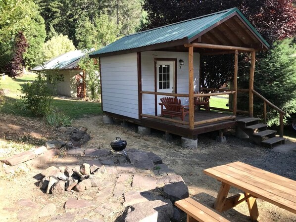 A small wooden cabin with a porch, a grill, and a picnic table.