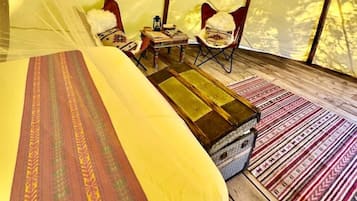 A tent with a bed, chairs, a small table, and a rug.